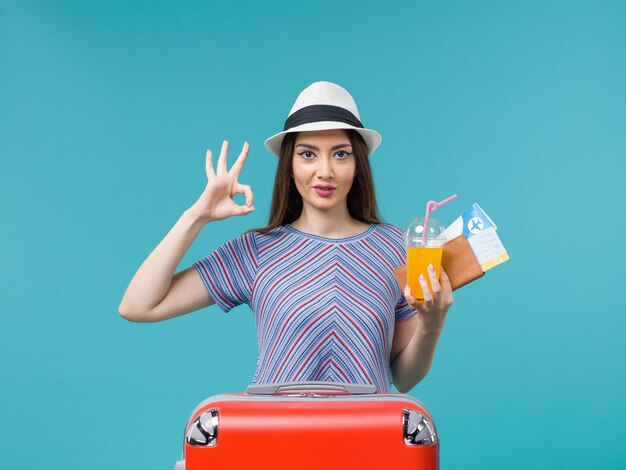 Mulher de férias com sua bolsa vermelha segurando os ingressos e suco em uma mulher de férias com fundo azul.