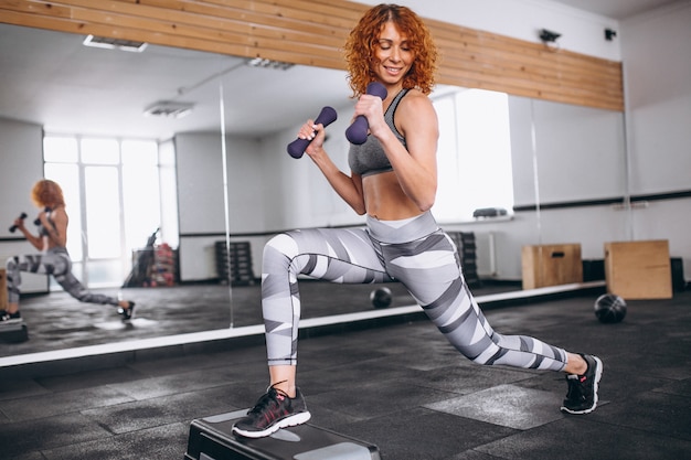 Mulher de fitness fazendo lunges com halteres no ginásio