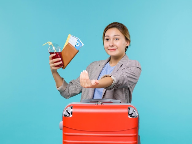 Foto grátis mulher de frente para as férias segurando suco e bilhetes chamando alguém no fundo azul viagem férias viagem viagem hidroavião