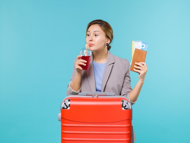 Mulher de frente para as férias segurando um copo de suco fresco e ingressos no fundo azul viagem avião férias viagem viagem mar