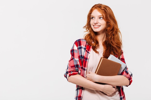 Mulher de gengibre satisfeito na camisa segurando livros e desviar o olhar