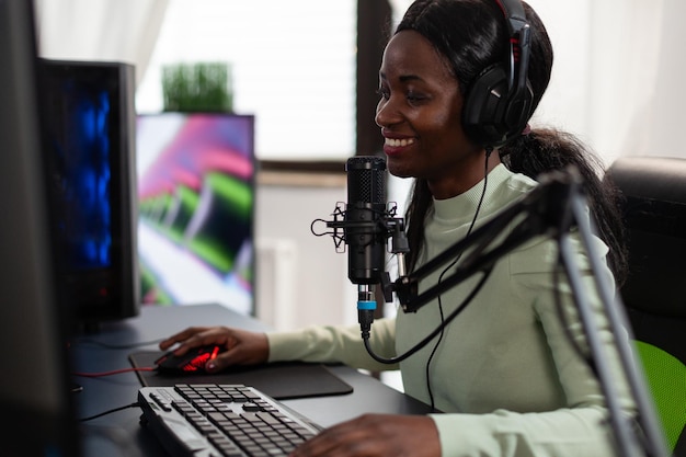 Mulher de jogador profissional concentrada falando no microfone com jogadores em transmissão ao vivo enquanto joga videogames de tiro espacial durante torneio online usando equipamento de computador RGB. E competição esportiva