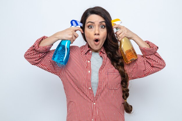 Mulher de limpeza muito caucasiana surpresa segurando produtos de limpeza em spray e olhando para a frente