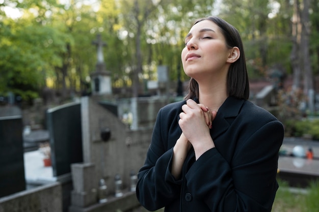 Mulher de luto rezando ao lado do túmulo no cemitério