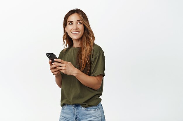 Mulher de meia-idade conversando, enviando mensagem de texto via smartphone, olhando para o lado com uma carinha sorridente e feliz