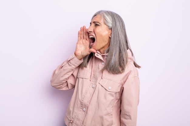 Mulher de meia-idade de cabelos grisalhos gritando bem alto e com raiva para copiar o espaço ao lado, com a mão perto da boca