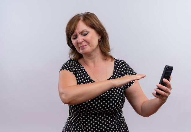 Mulher de meia-idade insatisfeita segurando um telefone celular e apontando para ele em um fundo branco isolado