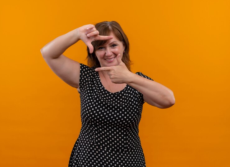 Foto grátis mulher de meia-idade sorridente fazendo gesto de fotografia em uma parede laranja isolada com espaço de cópia