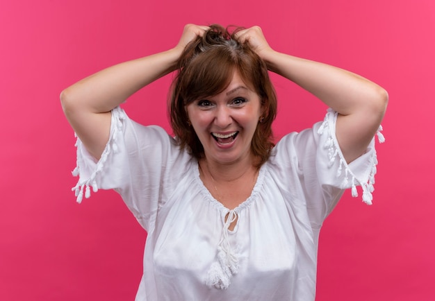 Mulher de meia-idade sorridente segurando o cabelo com as mãos na parede rosa isolada