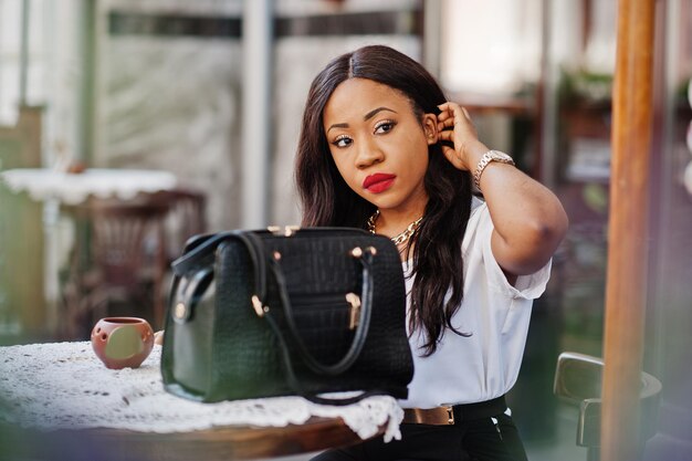 Mulher de negócios afro-americana elegante sentada no café ao ar livre com telefone celular