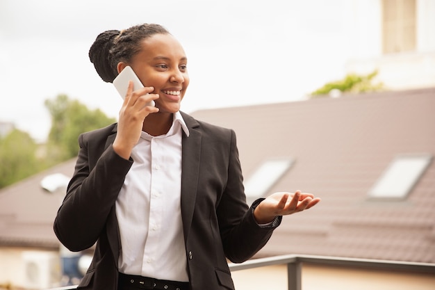 Mulher de negócios afro-americana em traje de escritório sorrindo, parece confiante e feliz, bem-sucedida