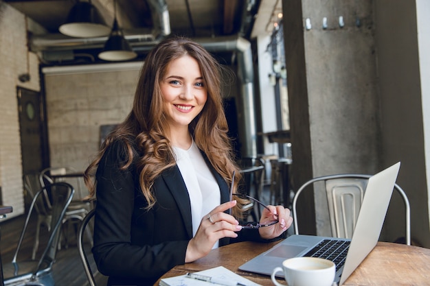Mulher de negócios amplamente sorridente trabalhando em um laptop sentada em um café