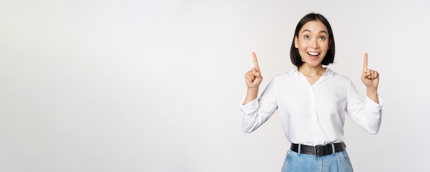 Mulher de negócios asiática entusiasmada apontando olhando para cima com rosto sorridente feliz mostrando o logotipo da empresa ou banner sobre fundo branco