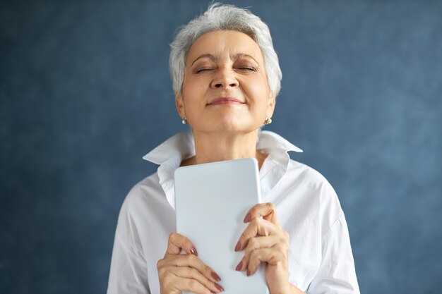 Mulher de negócios bem parecida com cabelos grisalhos fechando os olhos de prazer, com uma expressão feliz