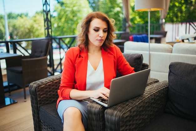 Mulher de negócios bem sucedida que usa o laptop ao sentar-se no café da sala de estar.