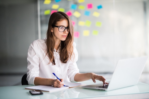 Mulher de negócios bem-sucedida trabalhando duro no laptop do escritório, vestida com roupas brancas