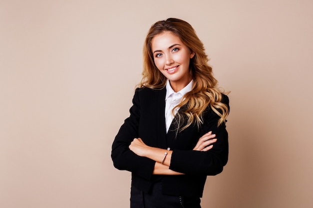 Mulher de negócios bem sucedido com sorriso sincero e braços cruzados em terno elegante na parede bege.