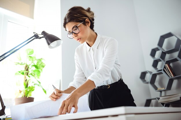 Mulher de negócios bonita nova que classifica através dos papéis no local de trabalho no escritório.