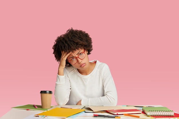 Mulher de negócios cansada, morena, estressada, sente dor de cabeça, parece cansada, mantém a mão na cabeça, usa um suéter branco casual