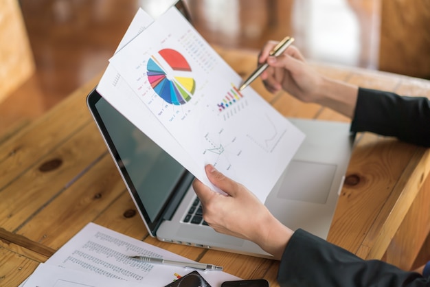 Mulher de negócios com gráficos financeiros e laptop na mesa.