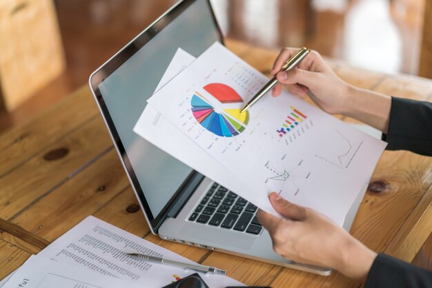 Mulher de negócios com gráficos financeiros e laptop na mesa.