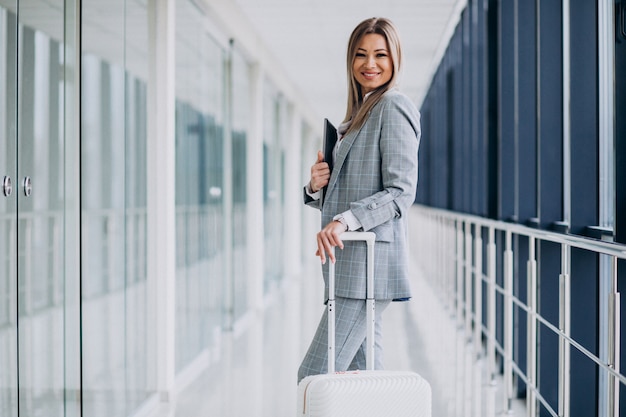 Mulher de negócios com malas de viagem no aeroporto, segurando laptop