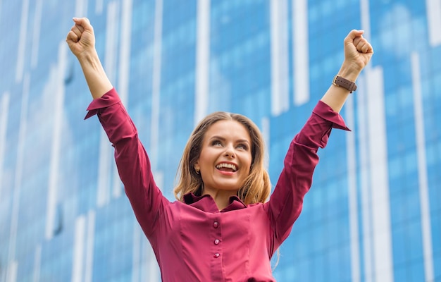 Mulher de negócios comemorando a vitória no centro da cidade. Moça bonita sorrindo com a mão levantada na frente de seu prédio de escritórios.