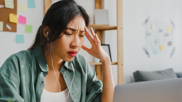 Mulher de negócios da Ásia usando laptop conversa com colegas sobre o plano de videochamada enquanto inteligente trabalhando em casa na sala de estar.