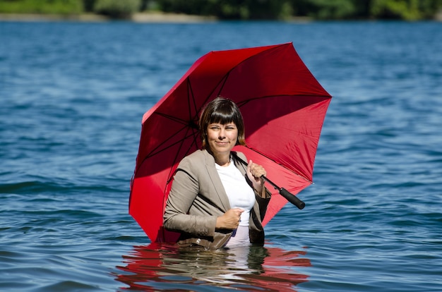 Foto grátis mulher de negócios de terno em pé na água segurando um guarda-chuva vermelho