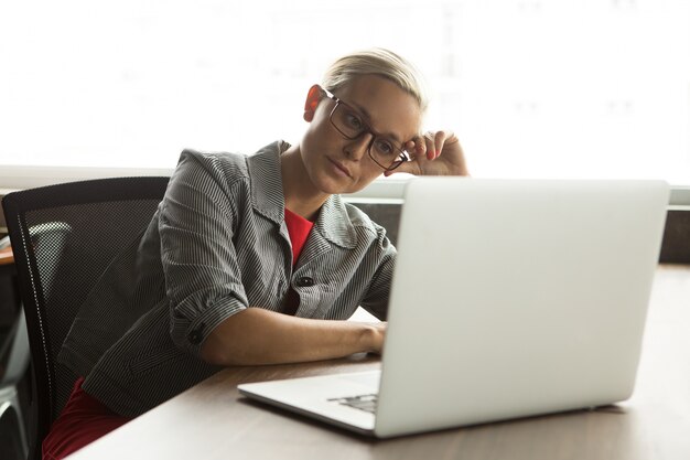 Mulher de negócios entediada em óculos que trabalham no laptop
