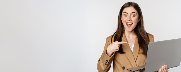 Mulher de negócios feliz apontando para a tela do laptop mostrando o progresso do trabalho e sorrindo animado em pé