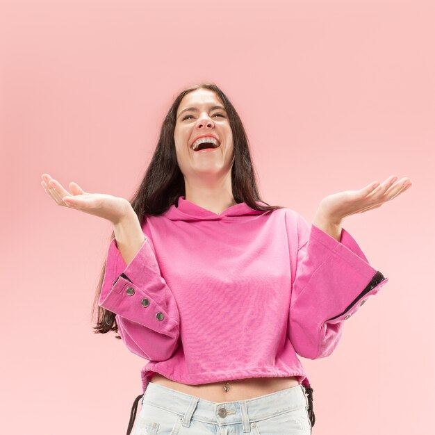 Mulher de negócios feliz em pé e sorrindo, isolado no fundo rosa do estúdio. Belo retrato feminino de meio corpo. Mulher jovem e emocional. As emoções humanas, conceito de expressão facial