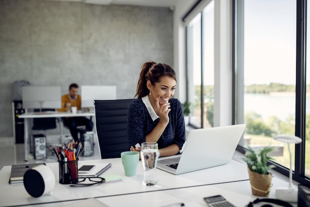 Foto grátis mulher de negócios feliz lendo algo na internet enquanto usa o computador no escritório