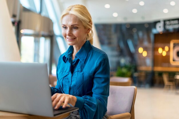 Mulher de negócios idosa sorridente trabalhando em um laptop enquanto está fora