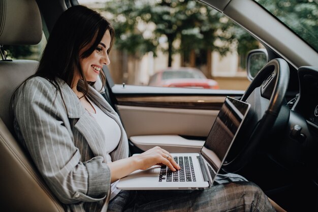 Mulher de negócios jovem bonita usando laptop e telefone no carro.