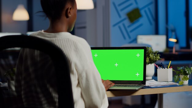 Mulher de negócios lendo no laptop com tela verde sentada à mesa no escritório à noite