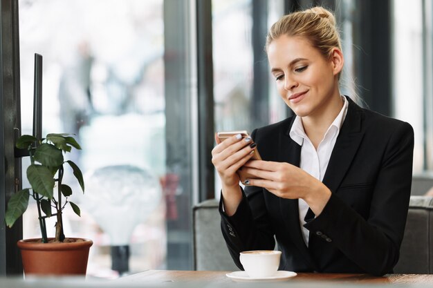 Mulher de negócios loira alegre usando telefone celular