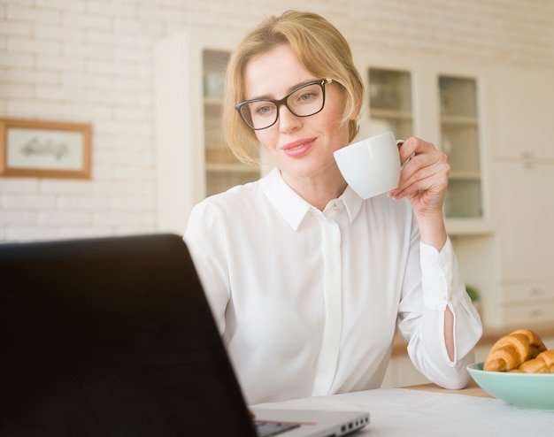 Foto grátis mulher de negócios loiro bebendo café enquanto estiver usando o laptop