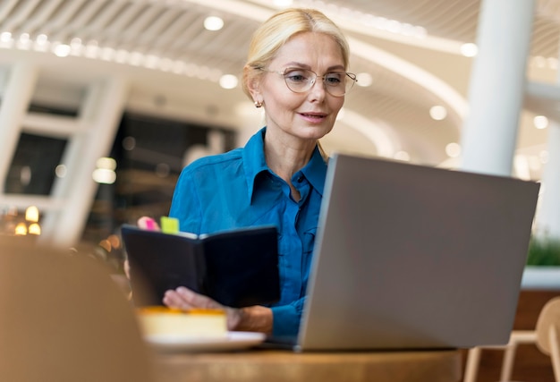 Mulher de negócios mais velha com óculos escrevendo na agenda e olhando para o laptop