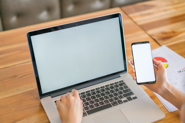 Mulher de negócios mão com gráficos financeiros e telefone celular sobre o laptop na mesa.