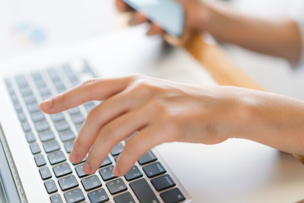 Mulher de negócios mão com gráficos financeiros e telefone celular sobre o laptop na mesa.