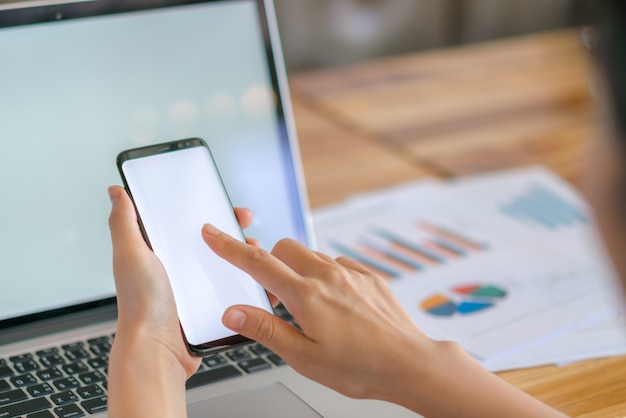 Mulher de negócios mão com gráficos financeiros e telefone celular sobre o laptop na mesa.