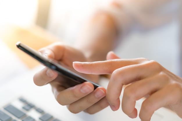 Mulher de negócios mão com gráficos financeiros e telefone celular sobre o laptop na mesa.