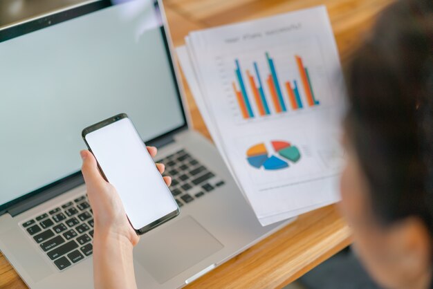 Mulher de negócios mão com gráficos financeiros e telefone celular sobre o laptop na mesa.