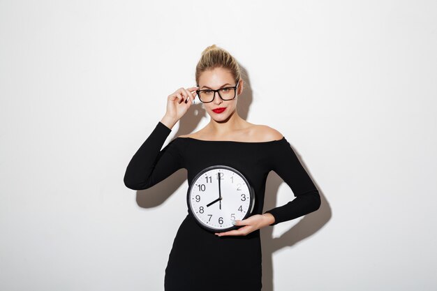 Mulher de negócios mistério no vestido e óculos segurando o relógio