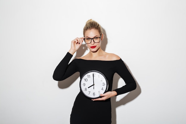 Mulher de negócios mistério no vestido e óculos segurando o relógio