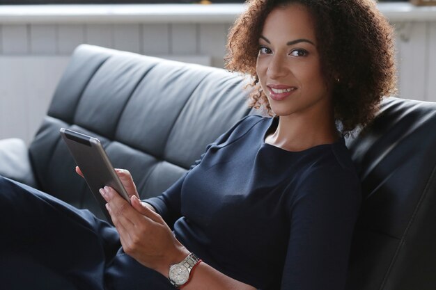 Mulher de negócios negra em um vestido preto estrito checando seus e-mails no tablet