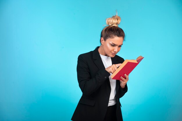 Mulher de negócios no blazer preto com um livro vermelho e lendo-o.