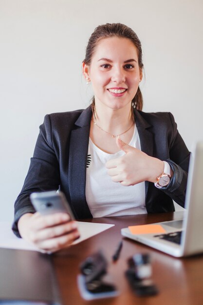 Mulher de negócios que gesticula polegar para cima no local de trabalho