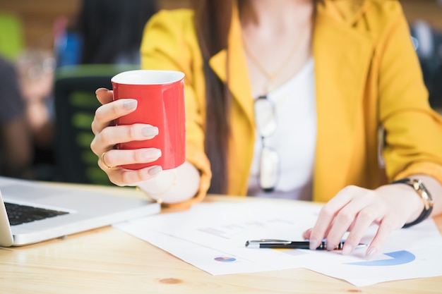 Mulher de negócios que segura uma xícara de café vermelha no tempo de coffeebreak.